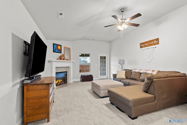 carpeted living room featuring lofted ceiling, a tile fireplace, visible vents, baseboards, and a ceiling fan