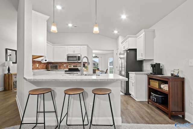 kitchen with stainless steel appliances, a peninsula, a sink, white cabinetry, and light countertops