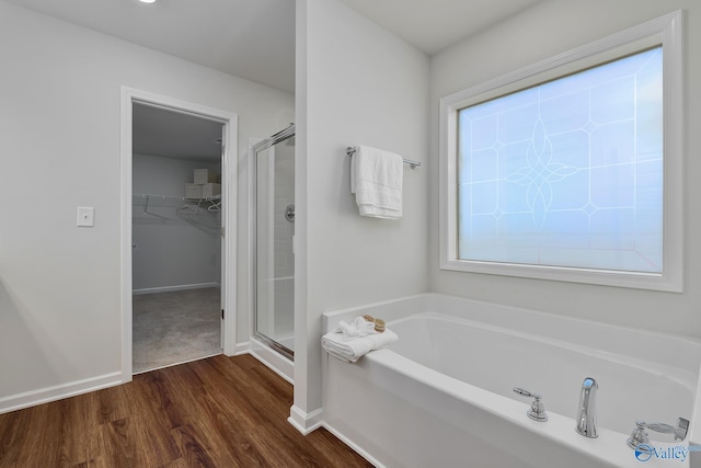 bathroom featuring wood finished floors, baseboards, a walk in closet, a bath, and a shower stall
