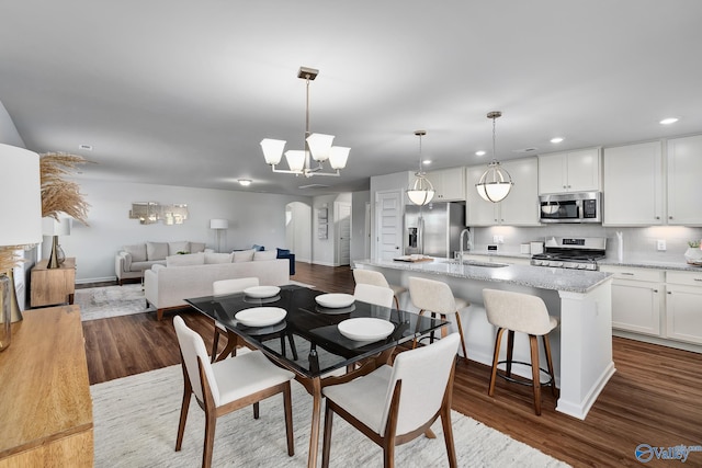 dining room featuring baseboards, recessed lighting, a chandelier, arched walkways, and dark wood finished floors