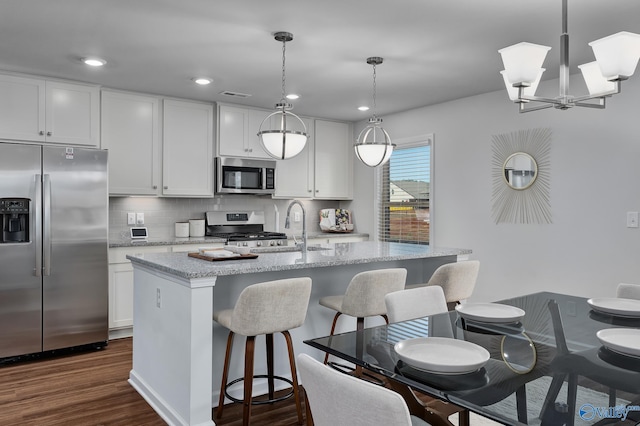 kitchen with appliances with stainless steel finishes, a sink, a center island with sink, decorative backsplash, and dark wood-style floors