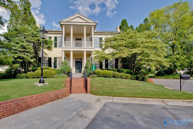 greek revival inspired property with a balcony and a front yard