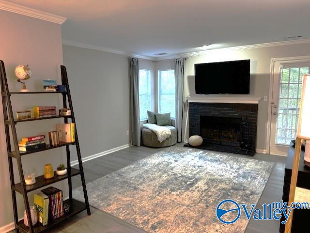 living room featuring hardwood / wood-style flooring, a healthy amount of sunlight, crown molding, and a brick fireplace