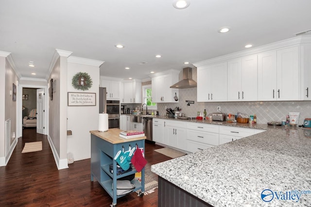 kitchen with tasteful backsplash, appliances with stainless steel finishes, a sink, white cabinetry, and wall chimney exhaust hood