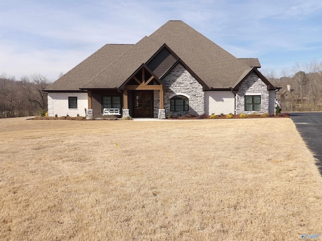 view of front of property featuring stone siding, a front lawn, and roof with shingles