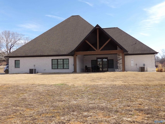 rear view of house with a yard, central AC unit, and a shingled roof