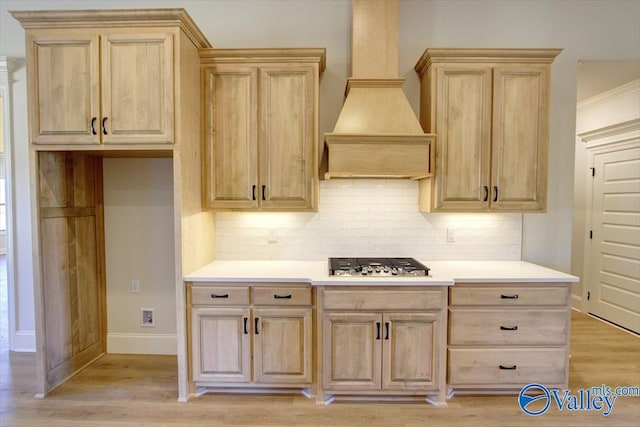 kitchen with premium range hood, stainless steel gas cooktop, light brown cabinets, light hardwood / wood-style floors, and decorative backsplash