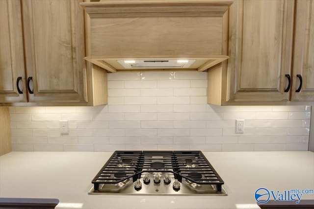 room details with decorative backsplash, light brown cabinetry, stainless steel gas cooktop, and custom range hood