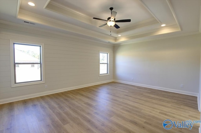 spare room with crown molding, a raised ceiling, and light wood-type flooring