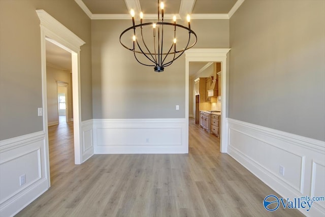 unfurnished dining area featuring an inviting chandelier, ornamental molding, and light hardwood / wood-style floors