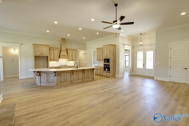 kitchen with built in microwave, an island with sink, custom exhaust hood, stainless steel oven, and light hardwood / wood-style flooring