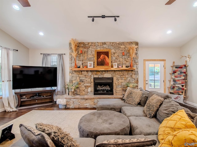 living room featuring lofted ceiling, dark wood-type flooring, a stone fireplace, rail lighting, and ceiling fan