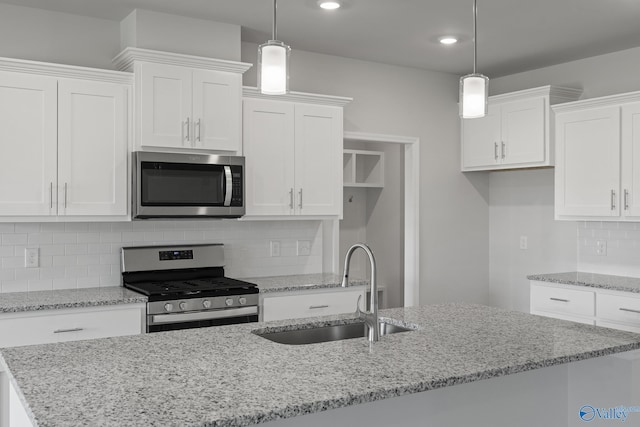kitchen featuring an island with sink, white cabinets, decorative light fixtures, stainless steel appliances, and a sink
