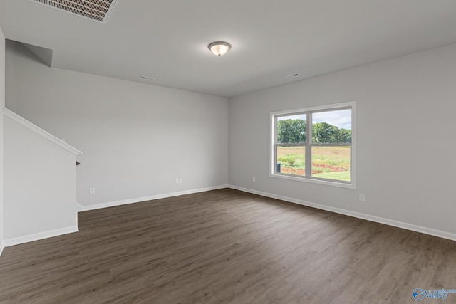 empty room featuring dark wood-type flooring, visible vents, and baseboards