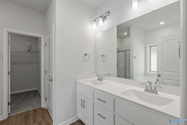 bathroom with a sink, a walk in closet, a stall shower, and wood finished floors