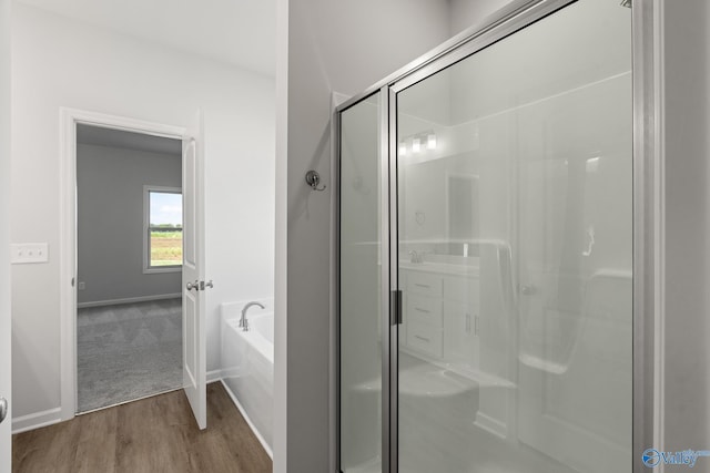bathroom featuring a stall shower, wood finished floors, baseboards, and a garden tub