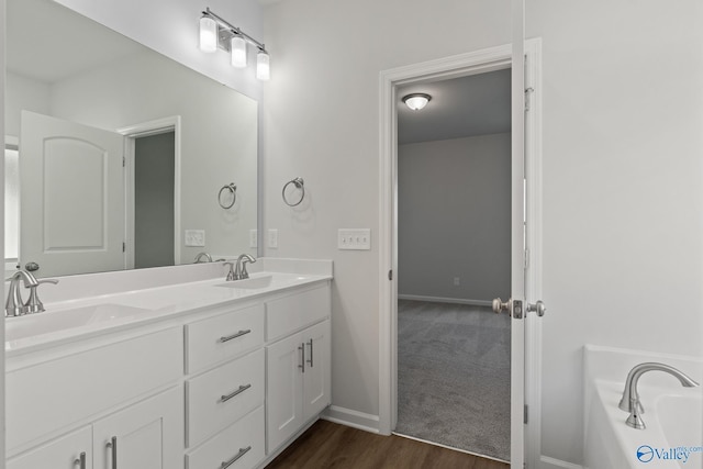 full bathroom with baseboards, double vanity, a sink, a garden tub, and wood finished floors