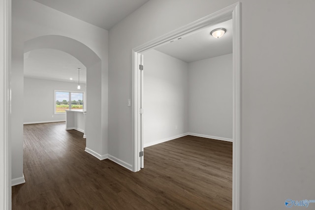 hallway featuring dark wood-style flooring, baseboards, and arched walkways