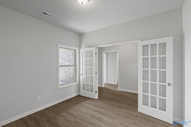 empty room with french doors, wood finished floors, baseboards, and visible vents