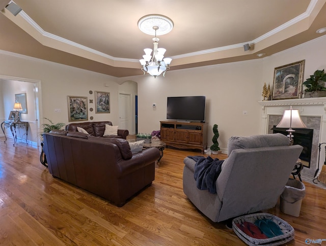 living room featuring a notable chandelier, a tray ceiling, ornamental molding, arched walkways, and wood finished floors
