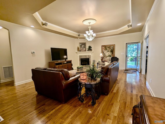 living area with a notable chandelier, visible vents, wood finished floors, and a tray ceiling