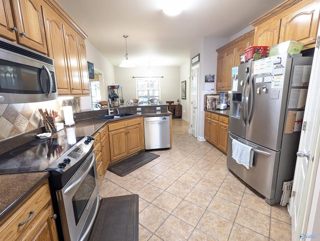 kitchen featuring light tile patterned floors, a sink, appliances with stainless steel finishes, dark countertops, and a peninsula