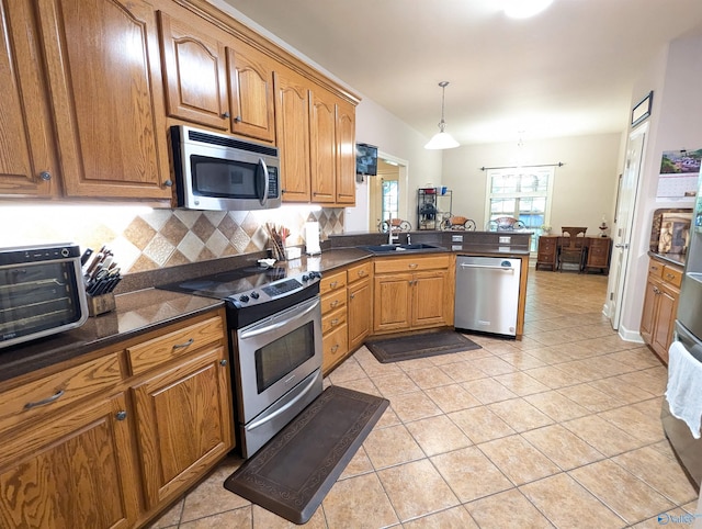 kitchen featuring decorative backsplash, a sink, dark countertops, stainless steel appliances, and a peninsula