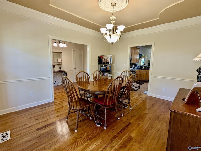 dining area featuring an inviting chandelier, crown molding, visible vents, baseboards, and wood finished floors