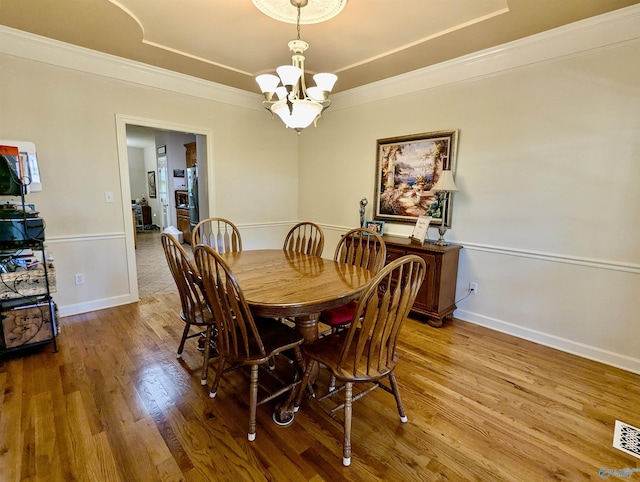 dining space with a raised ceiling, wood finished floors, a notable chandelier, and crown molding