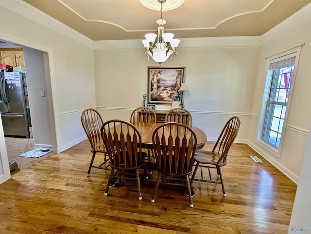 dining area with crown molding, light wood finished floors, a notable chandelier, and visible vents