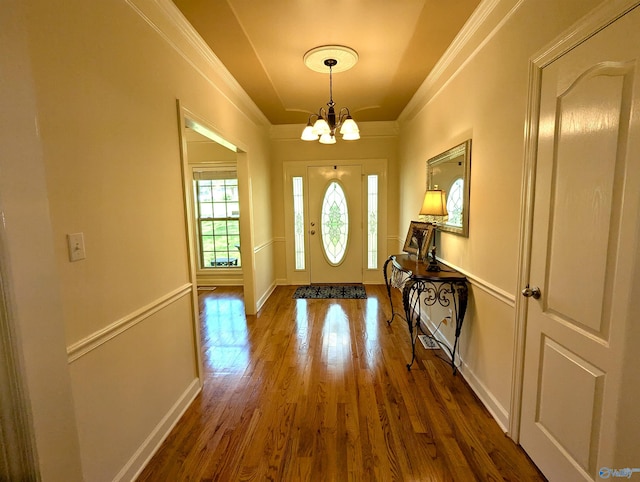 entrance foyer with dark wood-type flooring, crown molding, a notable chandelier, and baseboards