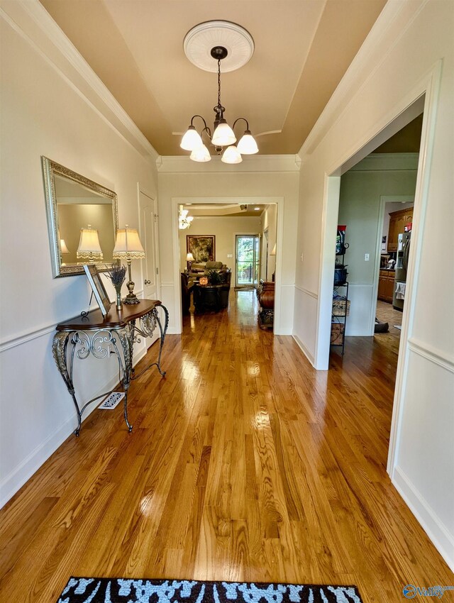 hall featuring an inviting chandelier, wood finished floors, and crown molding