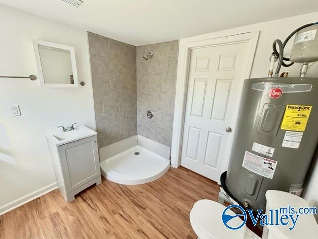 bathroom with a tile shower, electric water heater, sink, hardwood / wood-style floors, and toilet