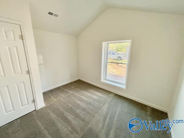 spare room featuring dark colored carpet and vaulted ceiling