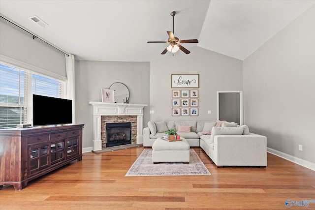 living room featuring ceiling fan, a stone fireplace, vaulted ceiling, and light wood-type flooring