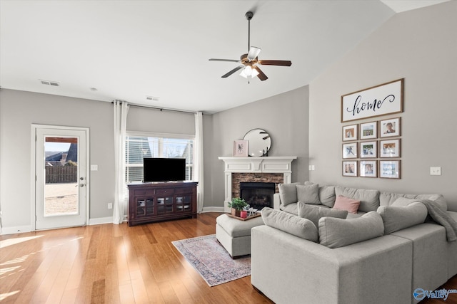 living room with lofted ceiling, a stone fireplace, light hardwood / wood-style flooring, and ceiling fan