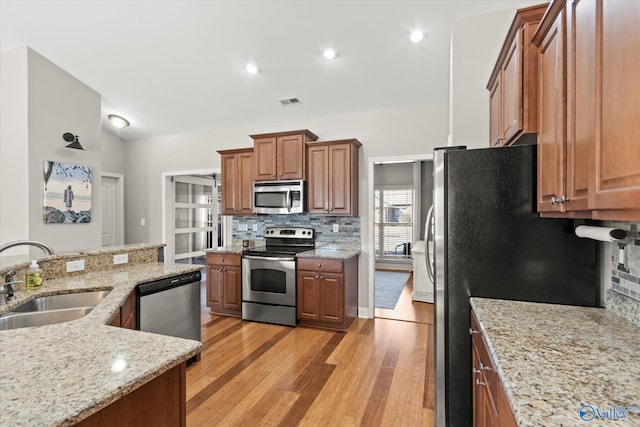 kitchen with sink, backsplash, light hardwood / wood-style floors, stainless steel appliances, and light stone countertops