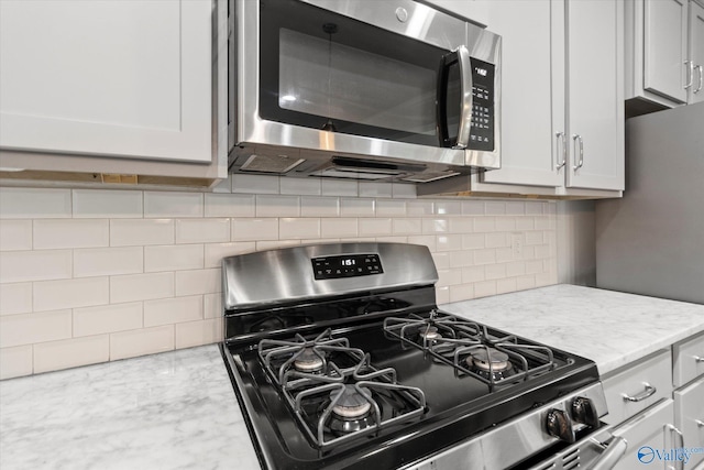 kitchen with decorative backsplash, light stone countertops, stainless steel appliances, and white cabinets