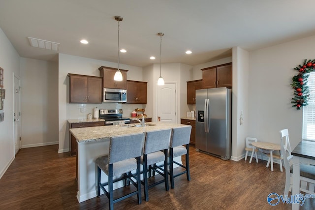 kitchen with a center island with sink, dark hardwood / wood-style flooring, pendant lighting, stainless steel appliances, and decorative backsplash