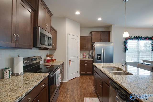 kitchen featuring sink, backsplash, stainless steel appliances, light stone countertops, and decorative light fixtures