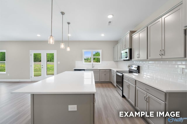 kitchen with a center island, gray cabinets, light countertops, backsplash, and appliances with stainless steel finishes