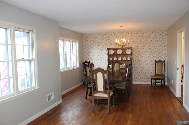 dining room with dark wood finished floors, a healthy amount of sunlight, a chandelier, and wallpapered walls