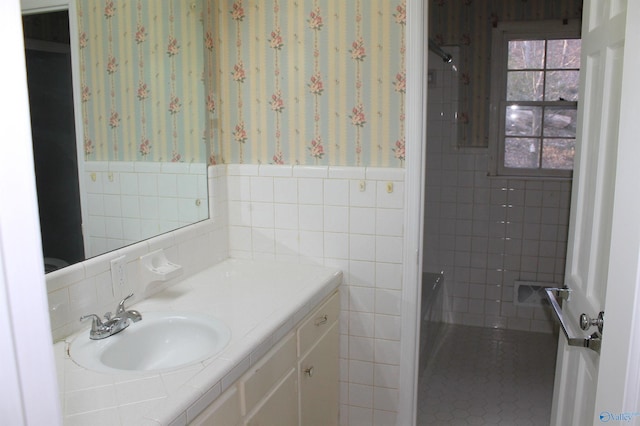 full bath featuring wallpapered walls, tile walls, vanity, and wainscoting