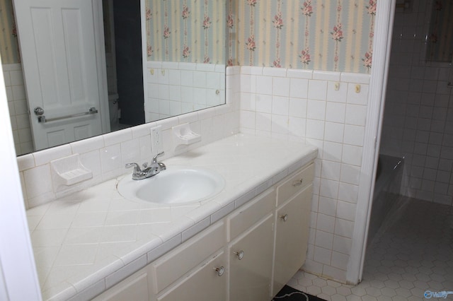 bathroom featuring wallpapered walls, tile walls, vanity, and wainscoting