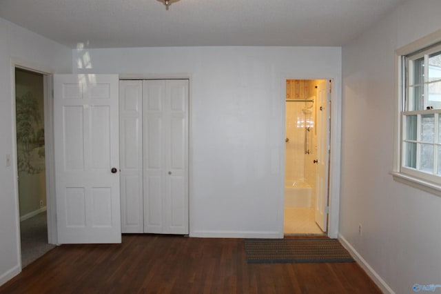 unfurnished bedroom with a closet, baseboards, dark wood-type flooring, and ensuite bathroom