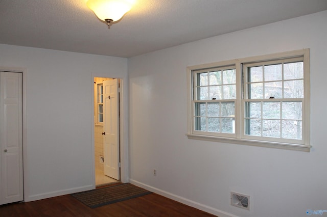 unfurnished bedroom with baseboards, multiple windows, visible vents, and dark wood-style flooring