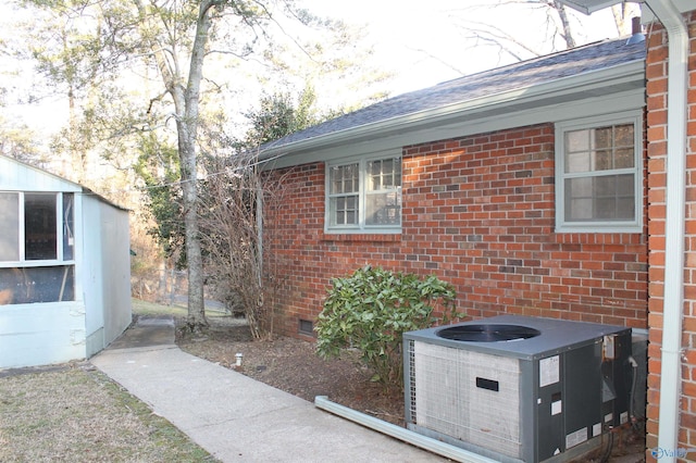 view of side of property with brick siding, crawl space, central AC unit, and a shingled roof