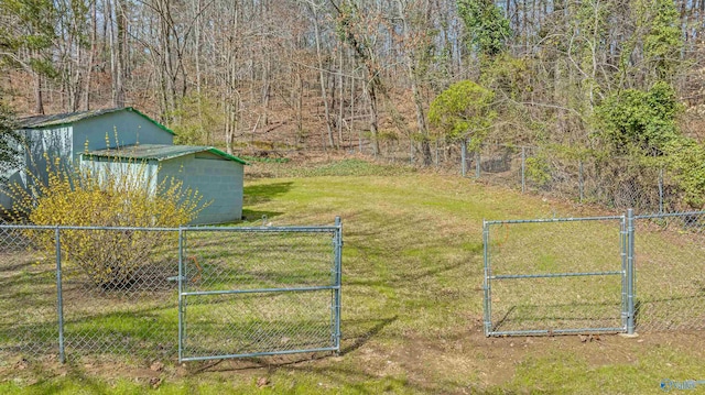 view of yard with a gate, a view of trees, an outbuilding, and fence