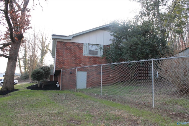 view of property exterior with brick siding, a yard, and fence