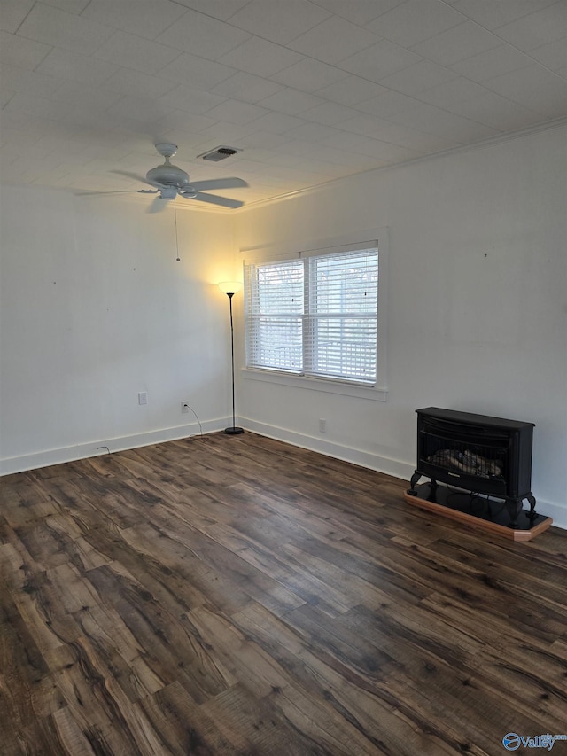 unfurnished living room with visible vents, a ceiling fan, dark wood-style floors, baseboards, and a wood stove